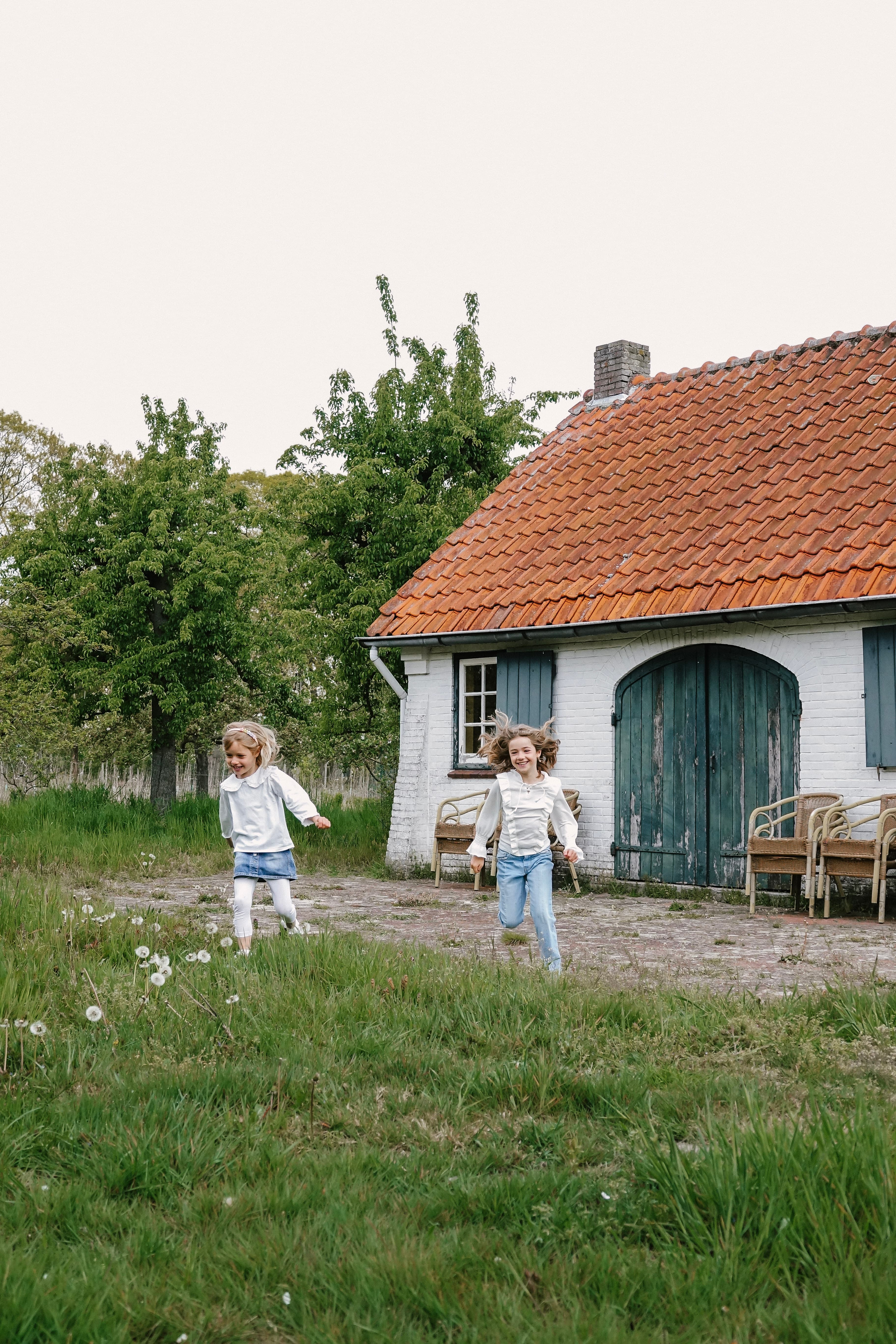 Twee meisjes rennen lachend voor een oude Brabantse boerderij